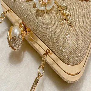 Gold glitter evening bag detail with pearl flower decoration and elegant chain strap for party.