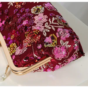 Close-up detail of dark red sequin evening bag with floral embroidery and gold metal frame.