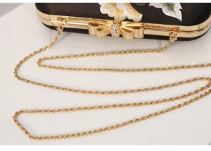 Elegant black evening clutch detail with floral embroidery, gold chain and rhinestone bow.