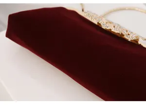 Detail close-up shot of a dark red velvet evening bag featuring an ornate rhinestone clasp.