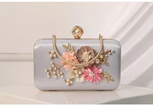 Detalle cercano del bolso de noche plateado con flores hechas a mano, perlas y asa metálica.