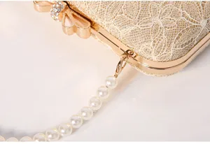 Close-up detail of luxury gold lace evening clutch bag with pearl chain and rhinestone bow.