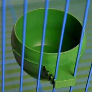 Detail view of the green plastic bird food bowl, showing clip-on design for wire birdcages.