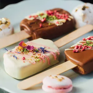 Close-up view of natural wooden popsicle sticks paired with decorated artisanal desserts.