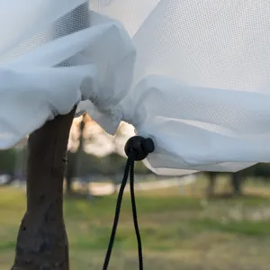 Close-up detail of white plant frost cover with adjustable drawstring and lock for winter tree protection.
