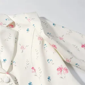 Close-up floral blazer detail, white fabric with pink roses and blue foliage, elegant resort style.