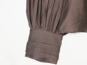 Close-up detail of women's long sleeve blouse cuff with pleated design in deep brown color.