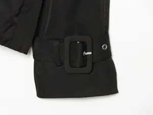 Black trench coat sleeve cuff detail with matching fabric buckle and metal eyelet trim.