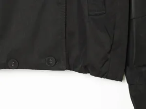 Close-up detail of women's black short trench coat showing hem buttons and pocket stitching.
