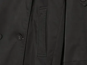 Close-up detail shot showing black trench coat pocket stitching and button craftsmanship.