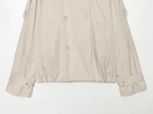 Close-up detail of women's beige short double-breasted trench coat cuff and button design.
