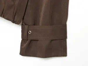 Close-up detail of trench coat sleeve cuff in chocolate brown with stylish buckle strap and eyelet.
