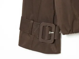 Brown trench coat sleeve detail with fabric buckle and metallic eyelet close up shot.