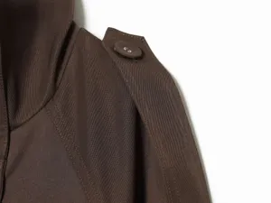 Women's short trench coat shoulder detail view, dark brown fabric with epaulette and button.