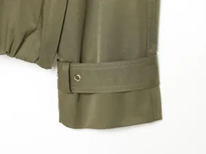 Detailed view of the olive green trench coat sleeve with buckled strap and metal eyelet.