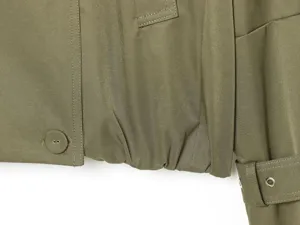 Detail shot of women's olive green cropped trench jacket hem, button and sleeve strap.