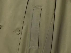 Close up detail view of women trench coat pocket, button stitching and green fabric.