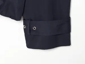 Detailed view of women's navy blue trench coat sleeve cuff with metal eyelets and buckle strap.
