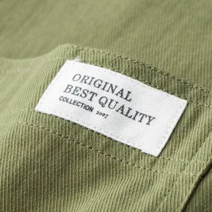 Close-up of green cotton fabric garment showcasing fine texture and custom woven brand label detail.