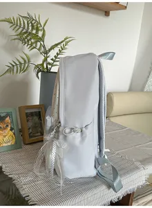 Light blue casual student backpack with side pocket and ribbon charm detail for daily wear.