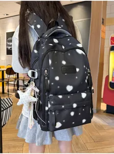 Detail view of a black backpack with white splatter heart prints being worn in a cafe.
