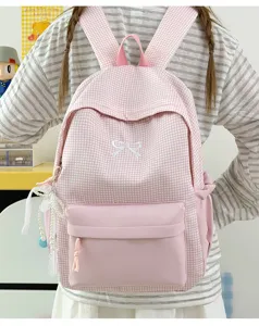 Détail de sac à dos à carreaux roses avec nœud mignon, pendentif perlé et poche avant.
