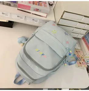 Light blue school backpack detail, featuring embroidered colorful stars and front zip pocket.