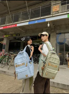 Outdoor street scene detail showing large letter canvas backpacks in light blue and green.
