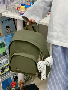 Detail view of a minimalist mini backpack in dark green with a polka dot bow pendant.