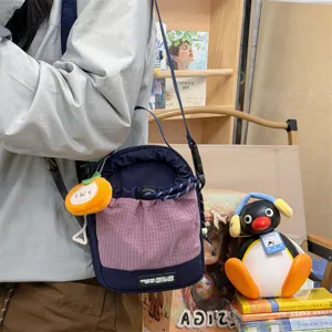 Stylish patchwork drawstring crossbody bag with cute orange pendant for outdoor travel.