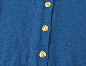Detailopname van een stijlvol blauw gebreid vest met elegante gouden metalen knopen.