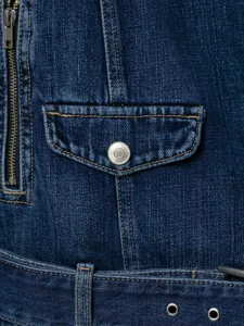 Detailopname van spijkerjas met metalen rits, borstzak en contrasterende stiksels.