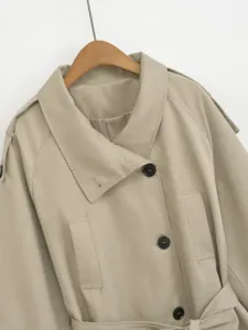 Classic beige trench coat detail showing wide lapel, black buttons and belt for women.
