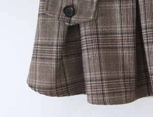 Detail view of brown plaid pleated skirt, featuring button flap and vintage style fabric texture.