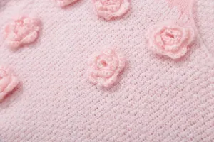 Nahaufnahme eines rosa Strickpullovers mit zarten 3D-Häkelrosenblumen-Details.