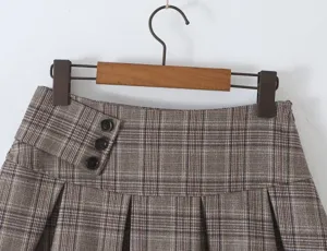 Detailed shot of a brown plaid pleated skirt with high waist and chic button accent.