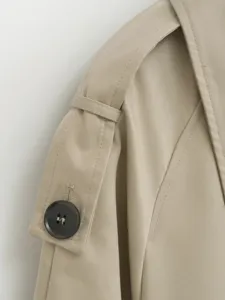 Close-up view of women's trench coat shoulder, featuring epaulet detail and dark button.