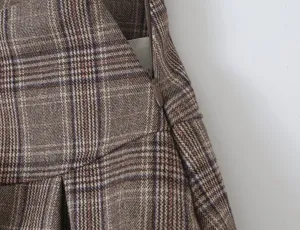 Close-up detail of women's brown plaid pleated skirt with side zipper, classic design.