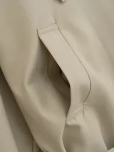 Close-up detail of women trench coat pocket, khaki twill fabric, fine stitching craftsmanship.