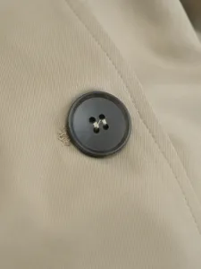 Close-up detail of a classic trench coat fabric and dark button, showing fine texture.