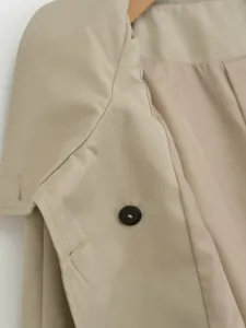 Close-up detail of women trench coat showing lapel, button, and smooth fabric texture.