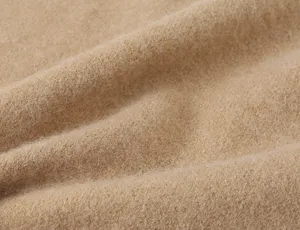 Close-up fabric detail of soft camel knitwear cardigan or vest, showing cozy fuzzy texture.
