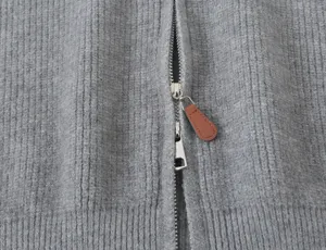 Gros plan détail de cardigan zippé en tricot côtelé gris pour femmes avec tirette cuir.