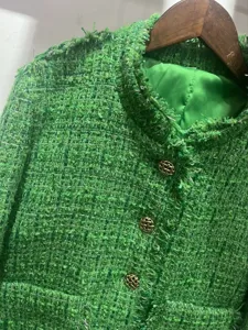 Close-up of elegant green tweed jacket with fringe details, chic metal buttons and smooth lining.