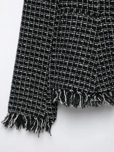 Close-up detail of black and white tweed blazer showcasing fringe hem and sleeve.