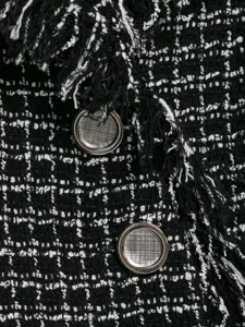 Black and white tweed blazer detail, classic textured fabric with stylish fringe and buttons.