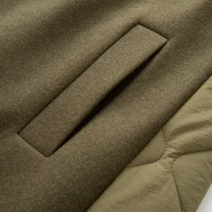 Olive green parka coat detail close-up showing pocket and wool fabric texture with quilted panel.