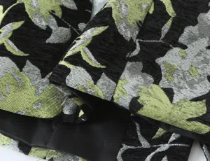 Close-up detail of women's fashion jacquard blazer fabric, elegant black and green floral pattern.