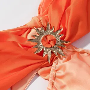 Nahaufnahme eines stylischen, orangefarbenen Gradient-Kleides mit goldener Sonnenschnalle.