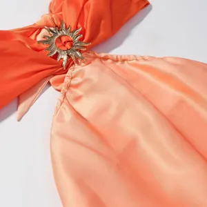 Nahaufnahme des orangen Farbverlauf-Kleidungsdetails mit goldener Sonnen-Metallschnalle.